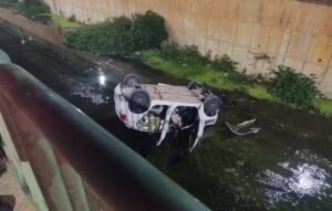 Carro capota em avenida e cai dentro de córrego